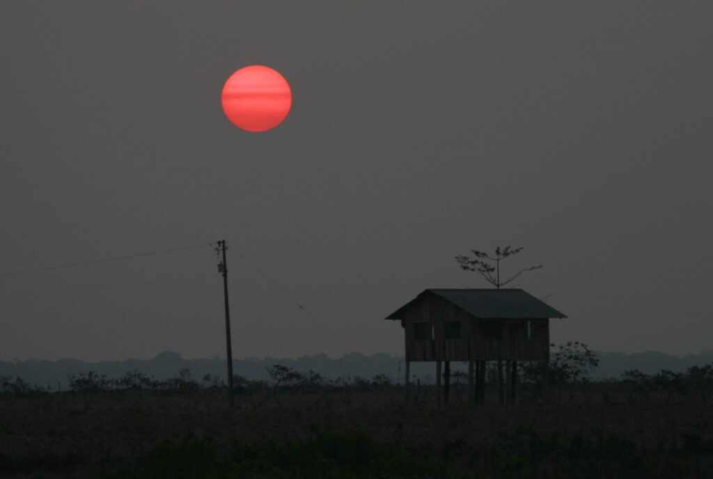 Sol vermelho no horizonte, perto de uma casa de palafita. Amazônia (ainda) queima