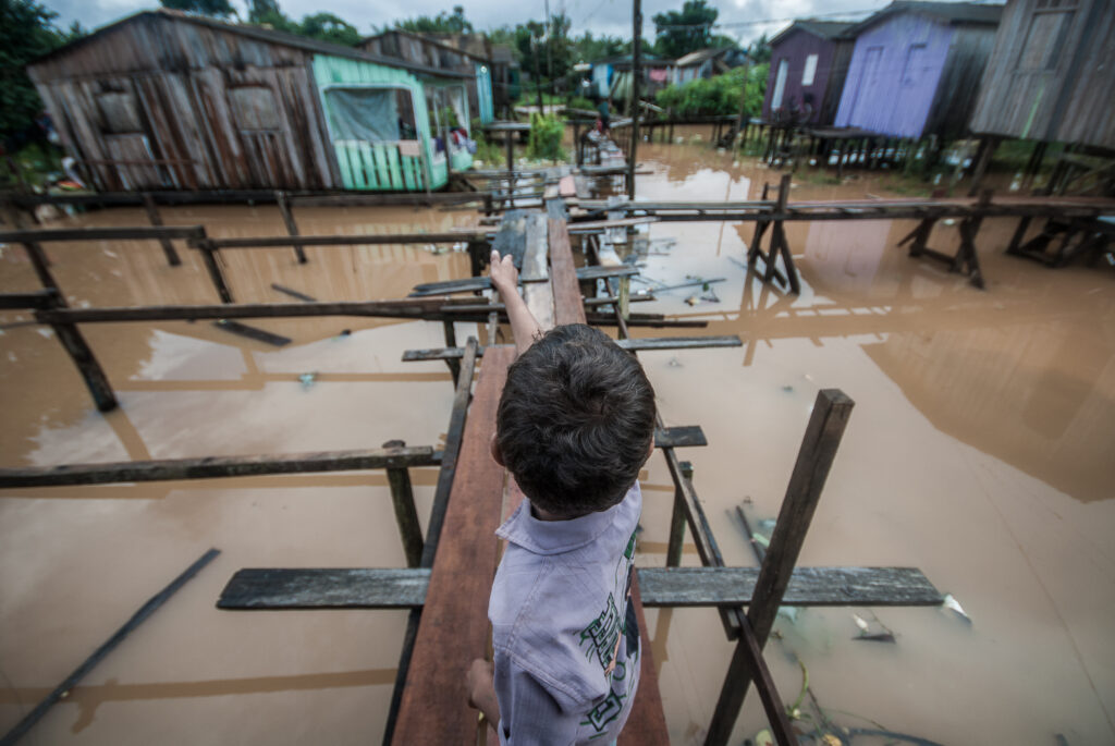 Um menino atravessa uma ponte improvisada que liga várias casas submersas em água marrom