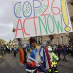 Um homem, envolto em bandeiras, segura no alto um cartaz em inglês COP26, act now