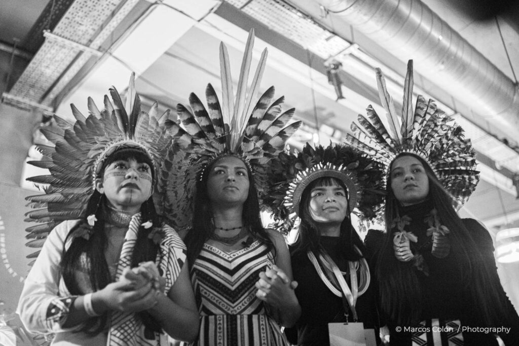 Foto em preto e branco de quatro indígenas jovens, vestindo suas roupas tradicionais 