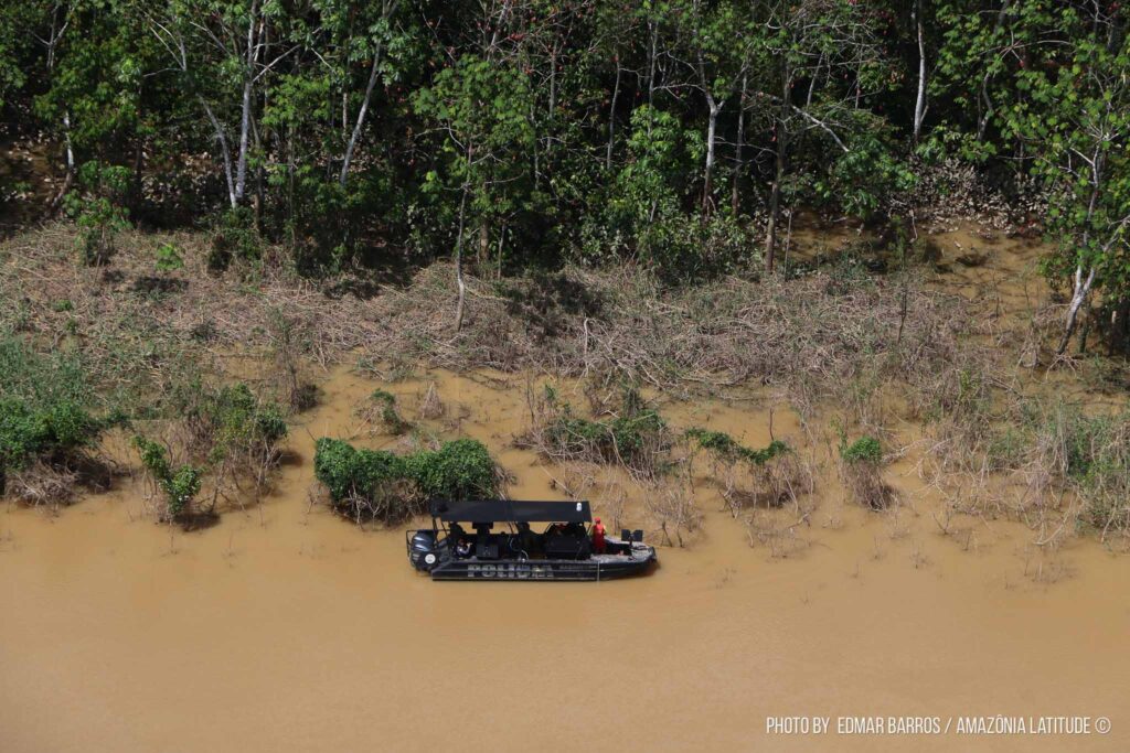 Foto de uma barco da polícia em um rio na beirada da floresta