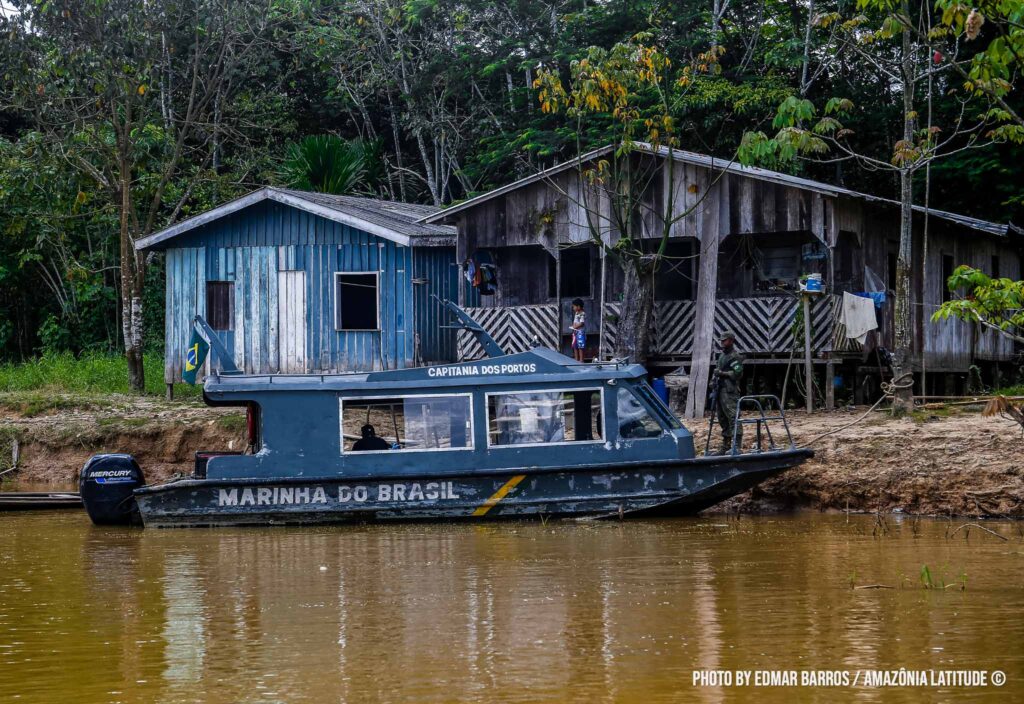Barco azul atracado em uma comunidade ribeirinha. No barco, está escrito: marinha do Brasil.