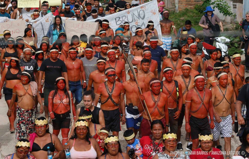 Grupo de indígenas, pintados de vermelhos, em uma rua protestando.
